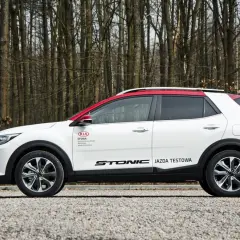 Biały Kia Stonic z czerwonym dachem, zaparkowany na tle lasu. Idealne kia stonic wymiary do miasta i na weekendowe wypady.