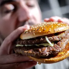 Mann hält einen saftigen Doppel-Cheeseburger mit Sesambrötchen. Perfekt für Burger Rezept Ideen!