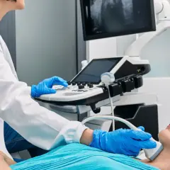 Lekarz wykonuje USG szyi pacjentki po operacji tarczycy, sprawdzając ewentualny ucisk krtani.
