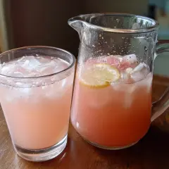 En glas och en karaff fyllda med rosa, isig dryck med citronskivor. Perfekt för enkla drinkar en varm dag.