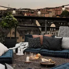 Gemütliches **outdoor wohnzimmer** auf einer Dachterrasse mit Blick auf die Stadt. Blaue Bodenkissen, Decken, Kerzen und eine Lichterkette schaffen Atmosphäre.