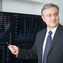 Mężczyzna w garniturze wskazuje na ekran z danymi finansowymi, wyjaśniając, kto płaci doradcy kredytowemu.