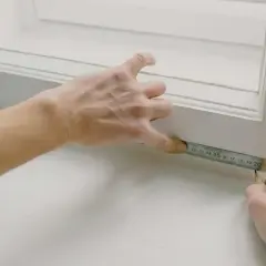 Ręce mierzą długość porysowanego parapetu z blachy.