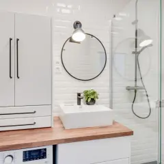 Coin buanderie dans salle de bain moderne avec machine à laver, lavabo, miroir rond et douche vitrée.
