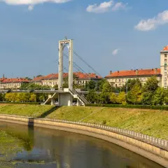 Most nowoczesny nad rzeką w Kownie starówka, z charakterystyczną wieżą i budynkami z czerwonymi dachami w tle.