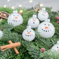 Schneemann-Weihnachtskugeln bemalen: süße Ideen für DIY-Deko. Tannengrün, Zimtstangen und getrocknete Orangen ergänzen die winterliche Szene.