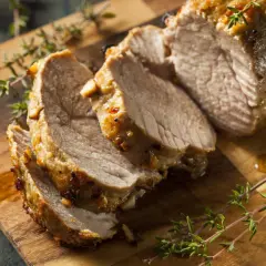 Tranches de filet mignon de veau rôti, juteux et savoureux, garnies de thym frais sur une planche à découper en bois.