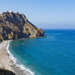 Costa rocosa con una playa de arena dorada y aguas turquesas. En lo alto del acantilado, casas blancas y un faro vigilan la costa. Un lugar idílico para disfrutar del sopalmo playa.