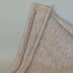 A close-up shows a grey fabric hem stitched with a twin needle, creating a decorative zigzag pattern.