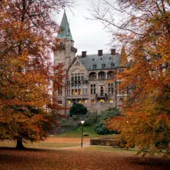 Växjö slott i höstfärger. Ett ståtligt stenbyggnad med torn och många fönster, omgivet av träd med orange löv.
