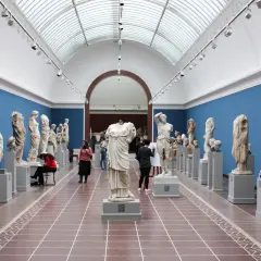 Wnętrze muzeum z rzeźbami antycznymi. Wśród zwiedzających artystka szkicująca posąg. Warto odwiedzić muzea w Krakowie.