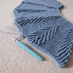 Maglia top down uncinetto in lavorazione, con un motivo a zig-zag e un uncinetto turchese.