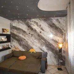 Soggiorno con divano, orologio a muro e una parete con una suggestiva texture pittura effetto marmo.