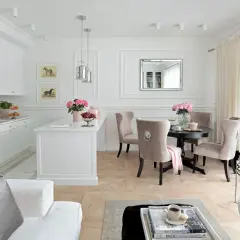 Elegancki salon z kuchnią inspiracje: białe meble, beżowe krzesła, okrągły stół, lustro, obrazy z końmi, kwiaty.