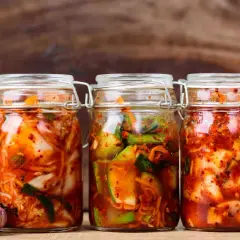 Drei Gläser mit koreanischer Vorspeise fermentierter scharfer Kohl (Kimchi) stehen bereit. Daneben liegen frische Zutaten wie Knoblauch, Ingwer und Limette.