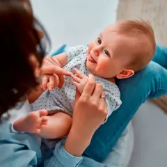 Madre juega con su bebé, enseñándole sus deditos. El bebé sonríe, quizás practicando sus primeras palabras.