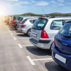 Rząd zaparkowanych samochodów na parkingu, z niebieskim samochodem na pierwszym planie.
