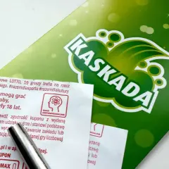 Zielona grafika z napisem KASKADA i fragmenty ulotki LOTTO. Zasady gry i odpowiedzialność.