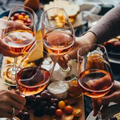 Różowe wino, czyli alkohol etylowy w jedzeniu, w kieliszkach na tle serów, owoców i przekąsek.