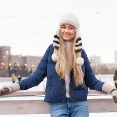 Uśmiechnięta kobieta w granatowej kurtce, futrzanej czapce i rękawiczkach na lodowisku.