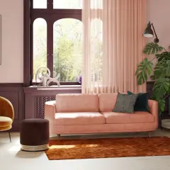 Ein pfirsichfarbenes Sofa mit modernen Kissen, umgeben von warmen Tönen, zeigt, welche Sofa Farbe ist modern. Ein gelber Sessel und ein brauner Hocker ergänzen den Look.