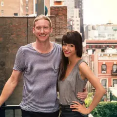 Jessica Walsh and her partner, perhaps celebrating a milestone in her most famous work, stand on a rooftop with a city skyline behind them.