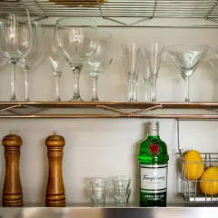 Czy bittersy (np. angostura) są niezbędne w domowym barku? Na półce stoją kieliszki, gin, cytryny i młynki do przypraw.