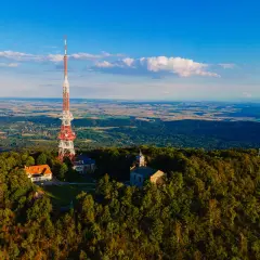 Wieża telekomunikacyjna na górze Ślęża góruje nad lasami i polami. Widać też budynki i kościółek.