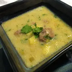 Aksamitna zupa porowo serowa z pulpecikami, ozdobiona natką pietruszki, w kwadratowej misce.