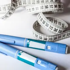 Dwa niebieskie peny GLP-1 i biała miarka krawiecka na białym tle.