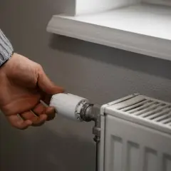 Dłoń regulująca termostat grzejnika w mieszkaniu.