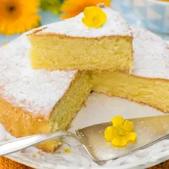 Una torta paradiso sofficissima, spolverata di zucchero a velo e decorata con un fiore giallo, pronta per essere gustata.