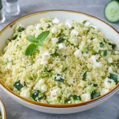 Frischer Couscous Salat mit Feta, Gurken und Minze, garniert mit einem Minzzweig.