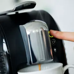 Finger drückt Knopf an Kaffeemaschine. Zeit, den Kaffeeautomaten zu entkalken für perfekten Kaffeegenuss.