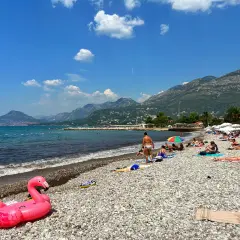 Plaża w Barze, Czarnogóra. Słoneczny dzień, ludzie odpoczywają na kamienistej plaży, a w tle widać góry. Atrakcje turystyczne tego miejsca przyciągają wielu wczasowiczów.