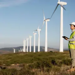 Inżynier w kamizelce odblaskowej i kasku obserwuje pracę wiatraków, analizując dane na tablecie. Tak działa turbina wiatrowa.
