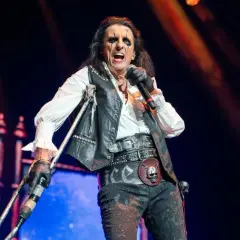 Alice Cooper na scenie z mikrofonem i kulami, w charakterystycznym makijażu i stroju.