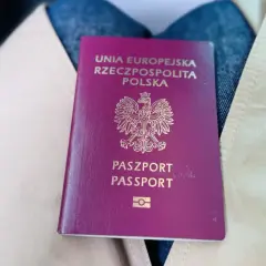 Polski paszport leżący na jasnym płaszczu i dżinsach.
