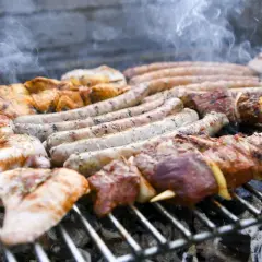 Des saucisses, brochettes de viande et morceaux de poulet à faire un barbecue sur un gril chaud, avec de la fumée qui s'échappe.