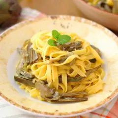 Tagliatelle fresche con carciofi teneri, guarnite con menta. Un piatto primaverile che celebra i sapori della terra.