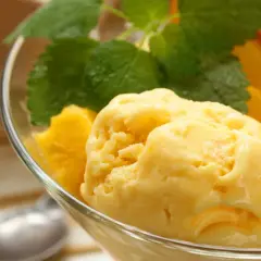 Domowe lody mango z miętą w szklanej miseczce.