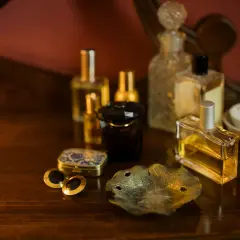 Eleganckie flakoniki z perfumami i woda kolońska co to? Na drewnianym blacie stoją różne rodzaje perfum, spinki do mankietów i ozdobna szkatułka.