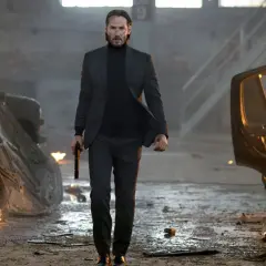 John Wick, med en pistol i handen, går genom ett inferno av brinnande bilar. En scen från rollistan i John Wick.