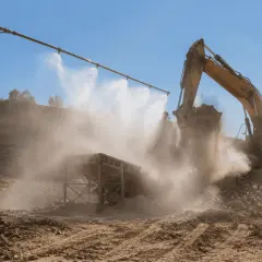 Excavadora amarilla trabajando en cantera, con sistema de desinfección por nebulización para controlar el polvo.