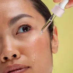 Kropla serum z pipetki spada na policzek kobiety. Czy retinol to witamina A? To pytanie nurtuje wiele osób dbających o cerę.