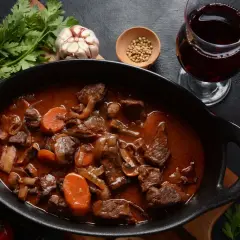 Un plat de bœuf bourguignon mijoté, avec carottes, champignons et oignons, accompagné d'un verre de vin pour bourguignon.
