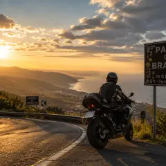 Motociclista ammira il tramonto sulle **strade panoramiche Liguria in moto**. Segnale del Passo del Bracco.