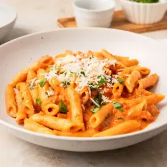 Penne alla vodka w kremowym sosie pomidorowym, posypane parmezanem i świeżą bazylią. Pyszne danie gotowe do podania.