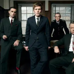 Fyra män i kostym och uniform står i ett kontor. En ung kommissarie Morse ser fundersam ut.
