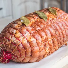 Gotowa do pieczenia pieczeń wieprzowa, związana sznurkiem i ozdobiona liśćmi laurowymi.